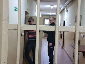 Policjant wprowadza podejrzanego do pomieszczenia dla zatrzymanych.