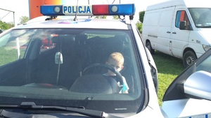 Dziecko ogląda radiowóz siedząc za jego kierownicą.