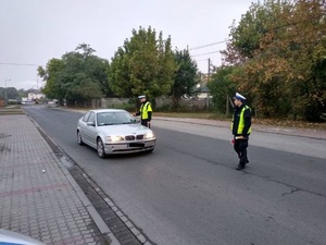 Policjant stoi na drodze i kontroluje stan trzeźwości kierowcy samochodu osobowego.