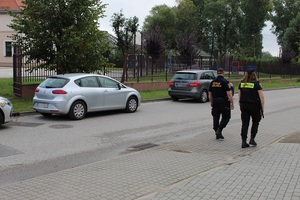 umundurowani strażnik i strażniczka miejscy pieszo patrolują ulicę przy szkole