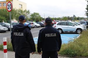dwaj umundurowani policjanci stoją patrząc w kierunku szkoły