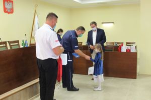 Komendant Policji w Kruszwicy pochyla się nad dzieckiem i podaje paczkę z nagrodami