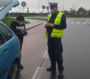 Policjant kontroluje kobietę i sprawdza jej dokumenty oraz to, czy nosi maseczkę