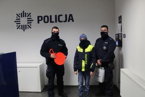 Na tle logo policji dzielnicowi stoją z chłopcem który jest laureatem konkursu